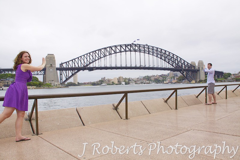 Couple pushing the pylons of Sydney Harbour Bridge together - engagement photography sydney